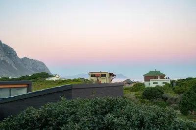 a house on a hill with mountains in the background at The Glass House Loft in Bettyʼs Bay