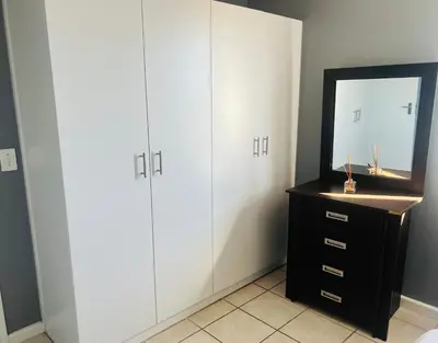 a bedroom with white cabinets and a mirror at Entire Modern, Secure & Central Flat in Milnerton in Cape Town