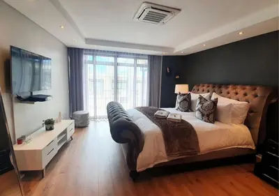 a bedroom with a large bed and a flat screen tv at Cape Town Sunset Beach Luxury Beachfront Villa in Cape Town