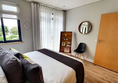a bedroom with a bed and a chair and a window at Cape Town Sunset Beach Luxury Beachfront Villa in Cape Town