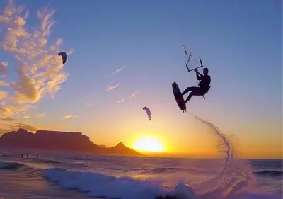 a man is in the air over the ocean with kites at Cape Town Sunset Beach Luxury Beachfront Villa in Cape Town