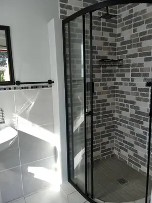 a glass shower in a bathroom with a brick wall at Paul's Place in Fisherhaven