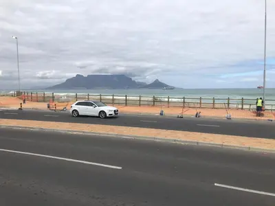 a white car driving down a road next to the ocean at Cape on Porterfield in Cape Town
