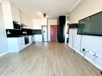a large kitchen with white cabinets and a large flat screen tv at Cape on Porterfield in Cape Town