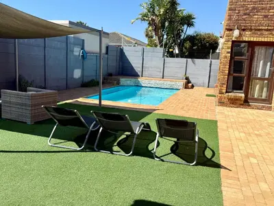 two chairs and a swimming pool in a yard at Hideaway-Poolside Comfort cottage 3km to the Beach in Cape Town