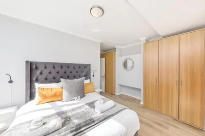 a white bedroom with a large bed and wooden cabinets at Horizon Bay 303-Oceanfront Apt on Kite Beach with Balcony & Pool in Cape Town
