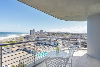 a table and chairs on a balcony with a view of the beach at Horizon Bay 303-Oceanfront Apt on Kite Beach with Balcony & Pool in Cape Town