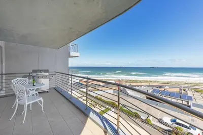 a balcony with a table and a view of the beach at Horizon Bay 303-Oceanfront Apt on Kite Beach with Balcony & Pool in Cape Town