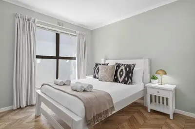 a white bedroom with a bed and a window at 17 Megans Place in Bloubergstrand