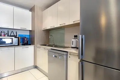 a kitchen with white cabinets and a stainless steel refrigerator at Beachfront Apt Kite Beach with Table Mtn View Horizon Bay 501 in Cape Town