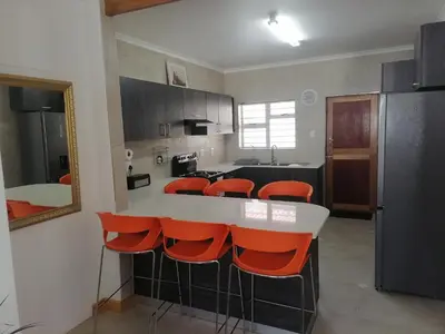 a kitchen with a white counter and orange chairs at Birds Nest Holiday Apartment in Zeekoevlei