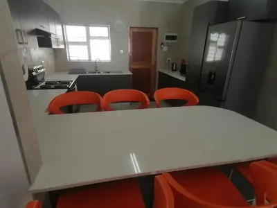 a kitchen with a white table and orange chairs at Birds Nest Holiday Apartment in Zeekoevlei