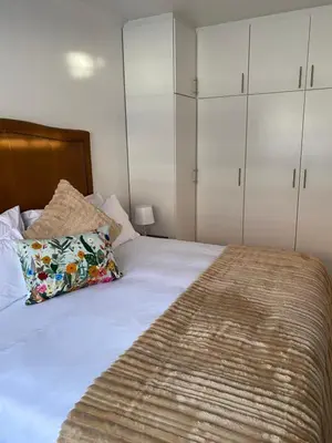 a bedroom with a bed with white cabinets at Birds Nest Holiday Apartment in Zeekoevlei