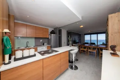a kitchen with wooden cabinets and a dining room at Beachfront Bliss with Table Mountain Views Horizon Bay 801 in Cape Town