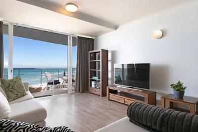 a living room with a couch and a television and a balcony at Chic Beachfront Apt with Table Mountain Views Horizon Bay 902 in Cape Town