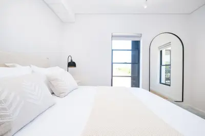 a white bedroom with a large white bed and a mirror at 221 Paarl Lux 1 Bdrm Apt with Mountain Views in Paarl