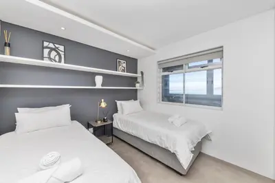 two beds in a room with a window at Modern Sea View Retreat with Pool & Inverter Horizon Bay 1405 in Cape Town
