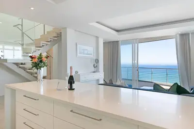 a white kitchen with a staircase and a living room at Horizon Bay 1602 Penthouse APT with lovely views in Cape Town