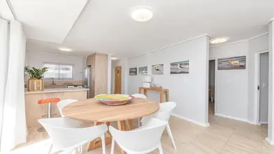a kitchen and dining room with a wooden table and white chairs at Lagoon Beach Gem 127 Pool, Views & Sea Breeze in Cape Town