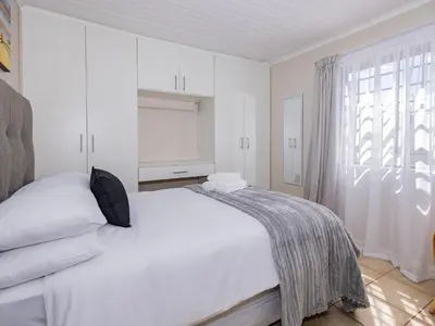 a white bedroom with a bed and a window at Urban Oaks in Bellville