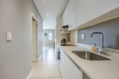 a white kitchen with a sink and a counter at Beach Break Bliss - Cozy retreat with mountain views in Bloubergstrand