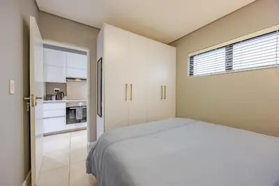 a small bedroom with a bed and a kitchen at Beach Break Bliss - Cozy retreat with mountain views in Bloubergstrand