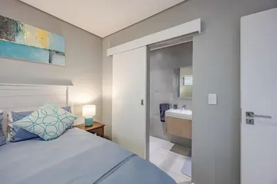a bedroom with a bed and a bathroom with a sink at Beach Break Bliss - Cozy retreat with mountain views in Bloubergstrand