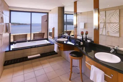 a bathroom with two sinks and a tub and a large window at Arabella Hotel, Golf and Spa in Kleinmond