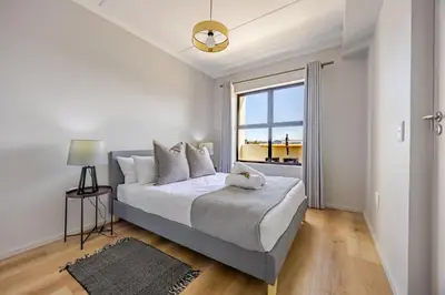 a white bedroom with a bed and a window at Contemporary Modern 1 Bedroom-19B, Blouberg in Cape Town