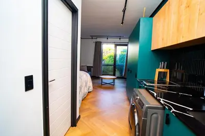 a room with a bed and a kitchen with green walls at Modern Studio Steps from Ratanga Park in Cape Town