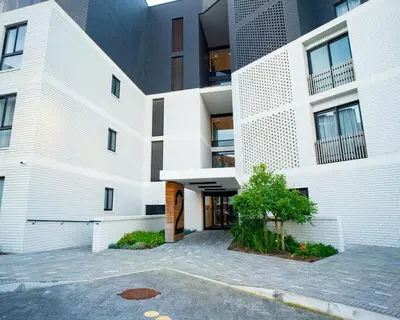 a white building with a parking lot in front of it at Modern Studio Steps from Ratanga Park in Cape Town