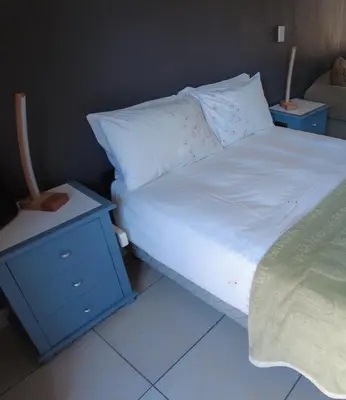 a bed with white sheets and a blue night stand at Studio Flat Bayside in Cape Town