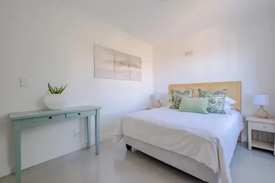 a white bedroom with a bed and a table at Serenity on 6th Luxury holiday home in Hermanus