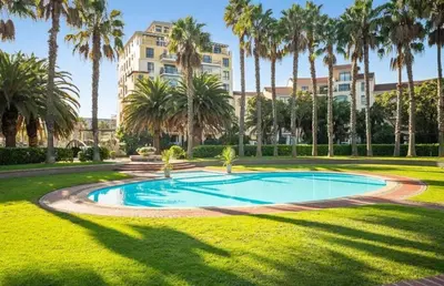 a swimming pool in a park with palm trees at Island Club Apartment in Cape Town