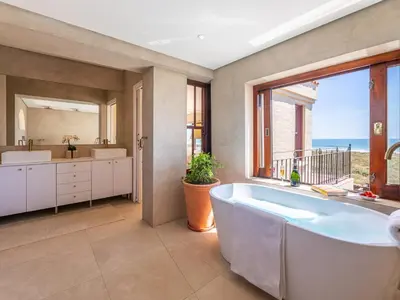 a bathroom with a tub and a large window at Luxury beachfront villa Cape Town - Sunset Beach in Cape Town