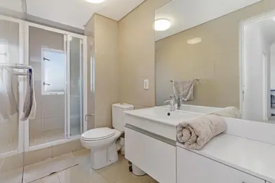 a white bathroom with a toilet and a sink at Stylish 2-Bedroom Sea-View Apartment Horizon Bay Blouberg Beachfront in Cape Town