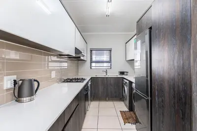 a kitchen with white counter tops and wooden cabinets at The Sandown 178 by CTHA in Cape Town