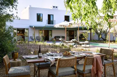 a table with chairs and a bottle of wine in front of a house at Spier Hotel and Wine Farm in Stellenbosch