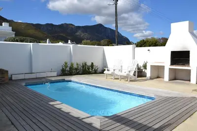 a swimming pool on a deck next to a house at Voëlklip House - Home with Pool & Mountain views in Hermanus