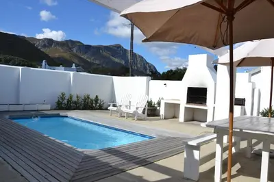 a swimming pool with a table and an umbrella at Voëlklip House - Home with Pool & Mountain views in Hermanus