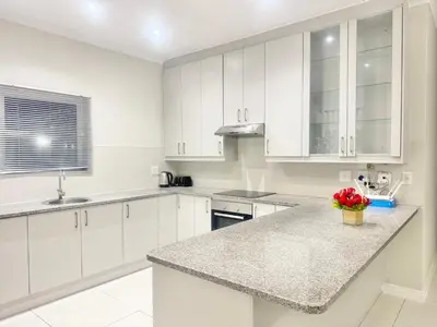 a white kitchen with white cabinets and a granite counter top at Villa Sunn in Cape Town