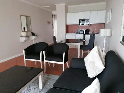 a living room with a couch and chairs and a kitchen at Cape Town Beachfront Apartments at Leisure Bay in Cape Town