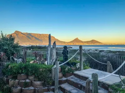 a person sitting on a staircase near the ocean at Cape Town Beachfront Apartments at Leisure Bay in Cape Town