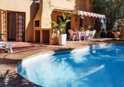 a swimming pool in front of a house with a table and chairs at Sunbird room in Cape Town