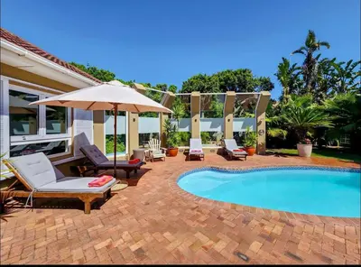 a patio with chairs and an umbrella and a pool at Sunset Bliss Villa, Sunset Beach, Cape Town in Cape Town