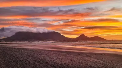 a sunset on a beach with a mountain in the background at Oh so Heavenly in Cape Town