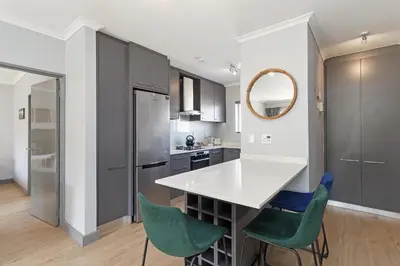 a kitchen with a white counter and green chairs at Dorphene 204 in Cape Town