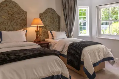 a bedroom with two beds and a lamp and two windows at La Petite Maison in Franschhoek