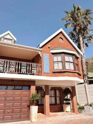 a red brick house with a garage and a palm tree at Nimara de So in Gordonʼs Bay