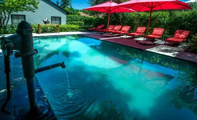 a swimming pool with red chairs and umbrellas at La Fontaine Boutique Hotel by The Oyster Collection in Franschhoek